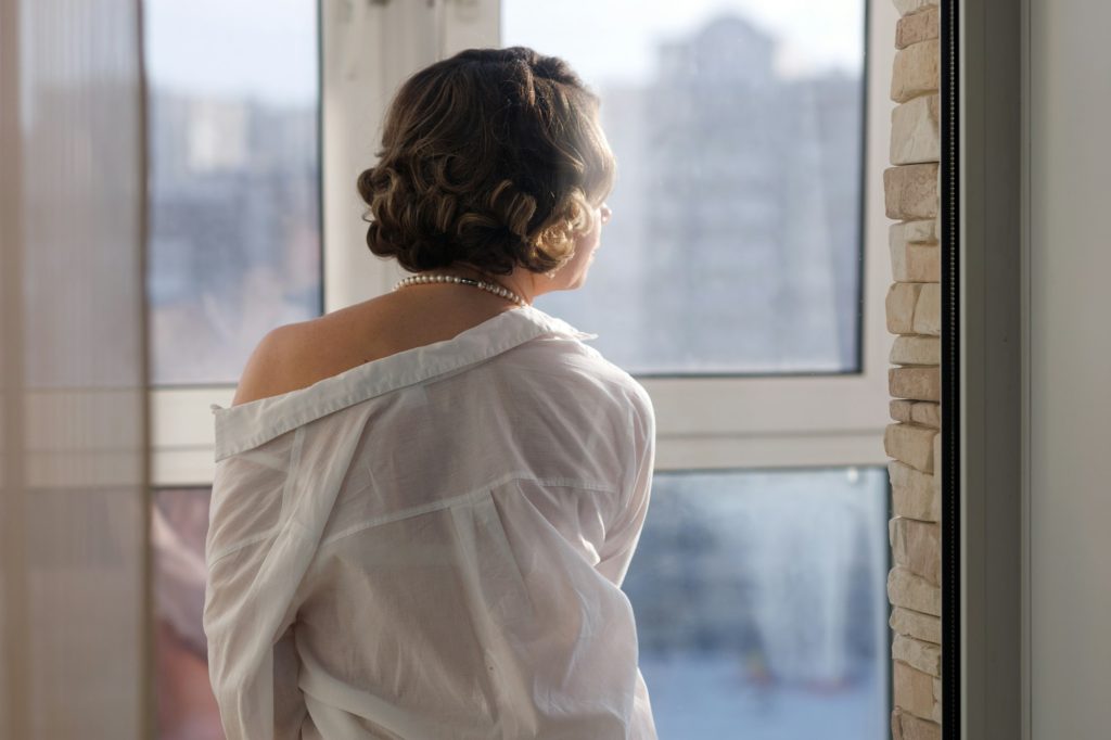 Beautiful girl in shirt on her naked body look thoughtfully out window after sex