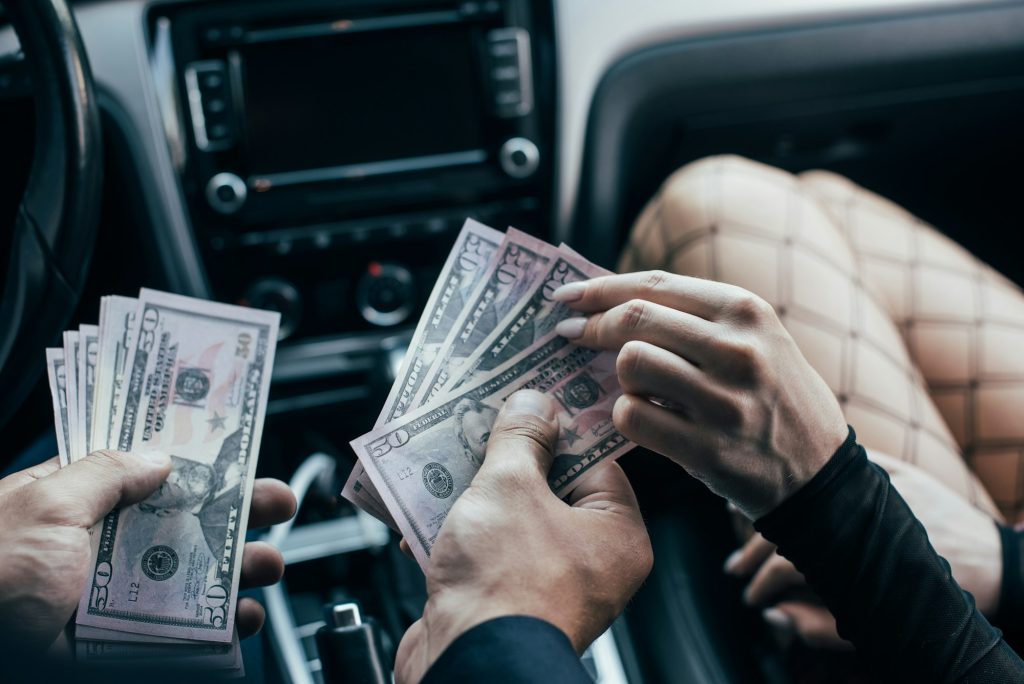 cropped view of client paying dollar banknotes to woman in car