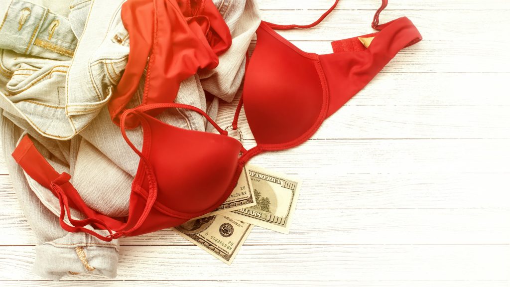 Red lingerie, jeans and money scattered on the floor. Love for money, prostitution concept