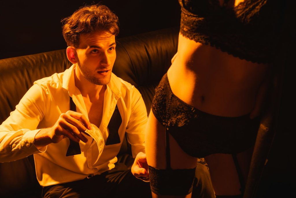 selective focus of man holding dollar banknote near seductive woman isolated on black