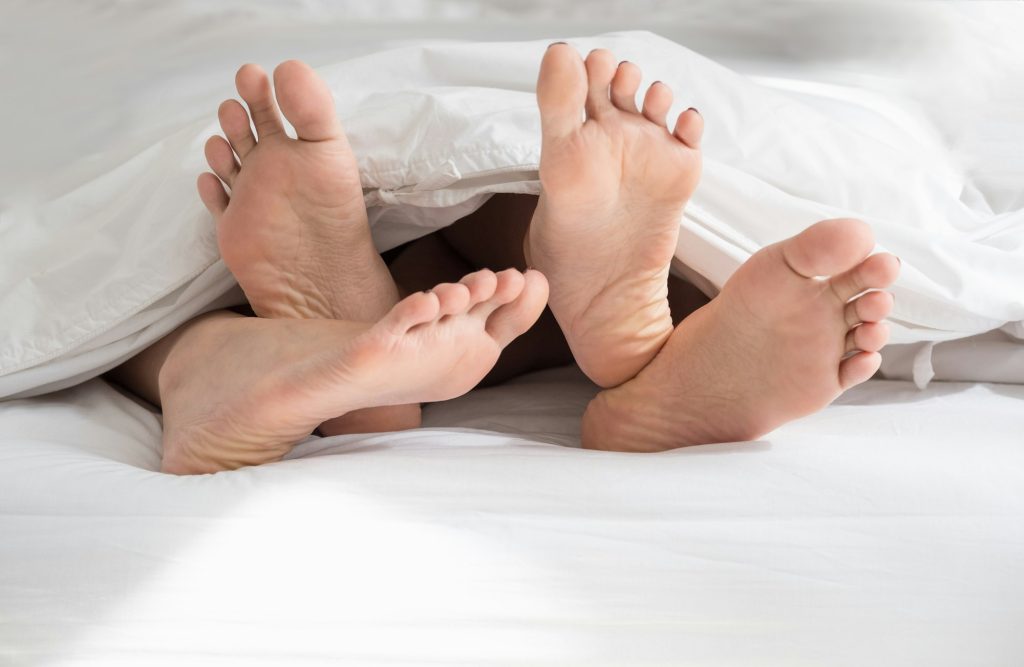 Close up barefoot legs of lesbian couple lovers sleep on white bed