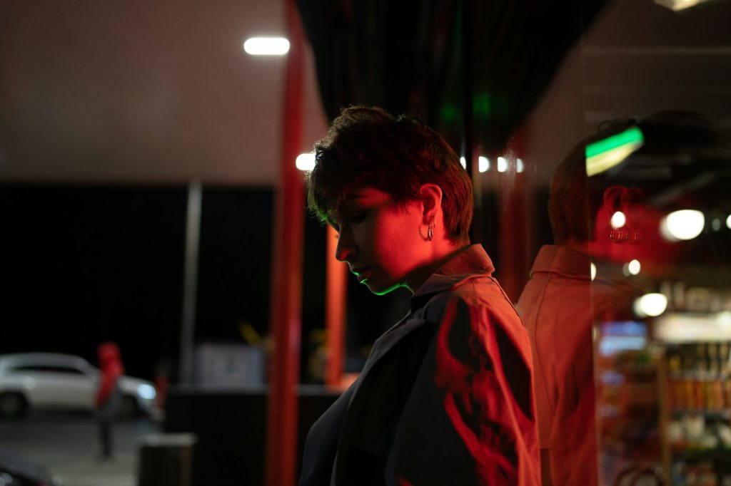 Pensive woman against glass wall on the street with red neon light at night. Sad and loneliness.