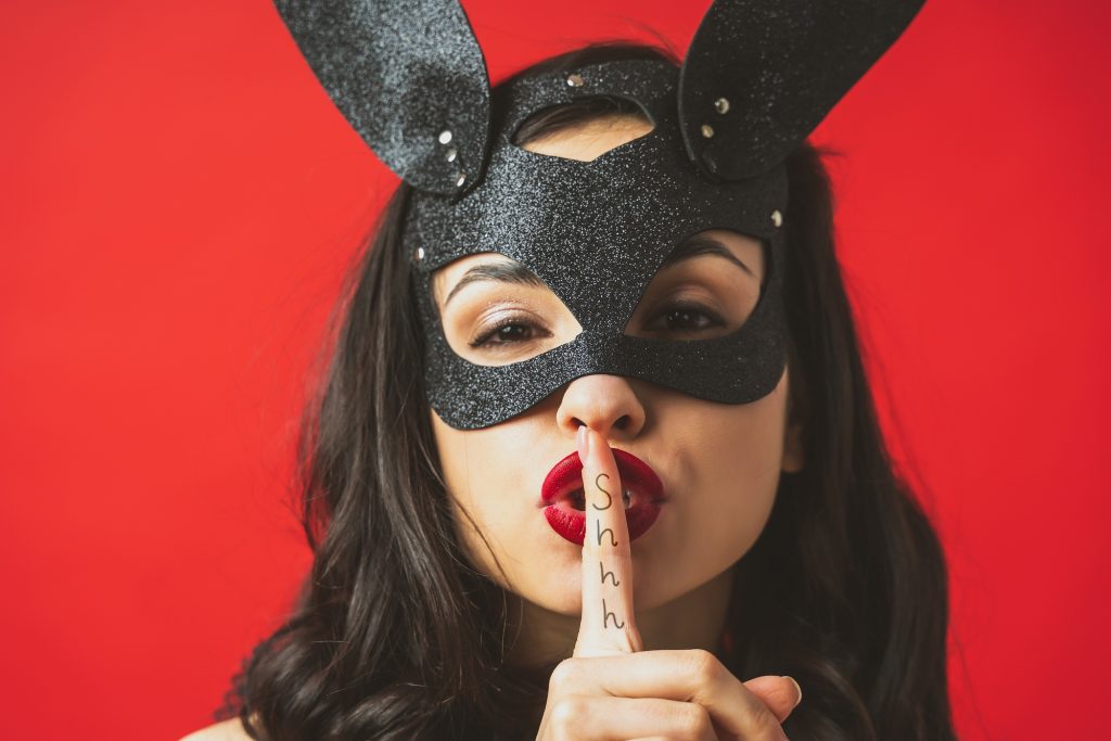 Image of a woman wearing a sexy rabbit mask and posing on a red colored background