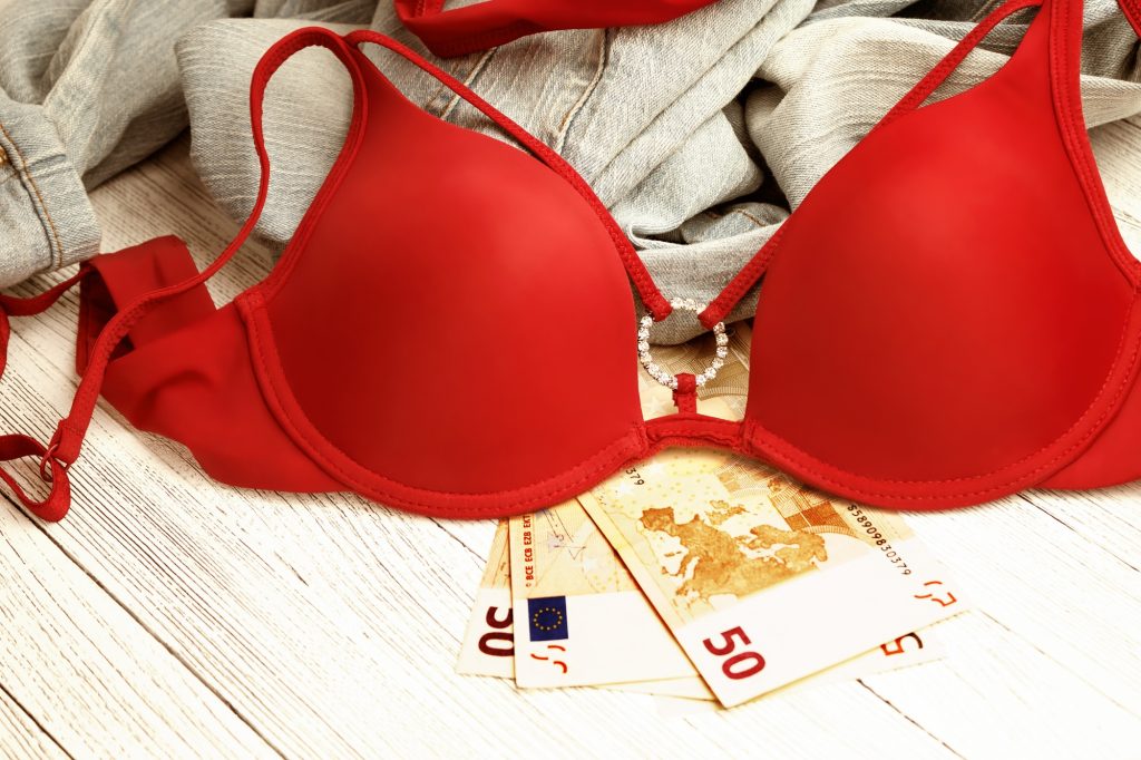 Red lingerie, jeans and money scattered on the floor. Love for money, prostitution concept